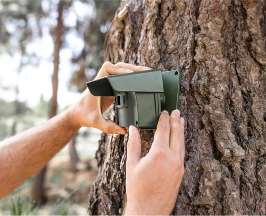 man setting up guardline wireless driveway alarm on a tree outside